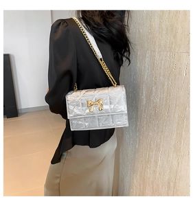 Details einer silbernen Stepptasche mit goldener Kette und Schleifenschnalle am Model
