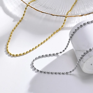 Detail of gold and silver olive bead necklaces layered on minimalist white marble