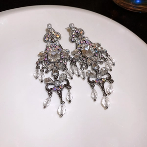 Close-up of vintage flower earrings with crystals, pearls and tassels on a white plate