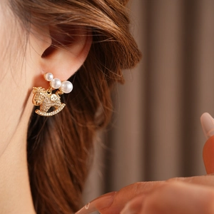 Détail d'une boucle d'oreille cheval à bascule dorée avec perles et diamants sur modèle
