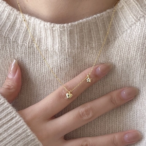 Close-up of a gold heart and star necklace with black stones on a knit sweater