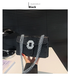 Detail of black faux crocodile leather crossbody bag with silver rhinestone buckle