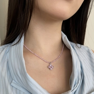 Detail of pink clover pendant necklace on model wearing a light blue striped shirt