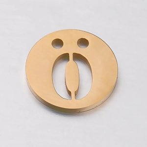 Gros plan d'un pendentif rond doré en acier inoxydable avec motif visage souriant évidé