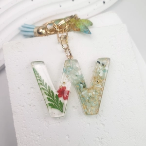 Detail of resin letter W keychain with green leaves, dried flowers and gold foil accents