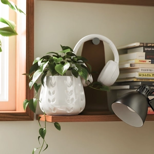 Detalle de maceta de cerámica blanca con corazones en relieve y plantas verdes frondosas