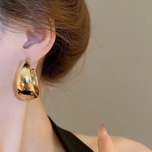 Close-up of a model wearing large glossy golden C-shaped acrylic hoop earrings