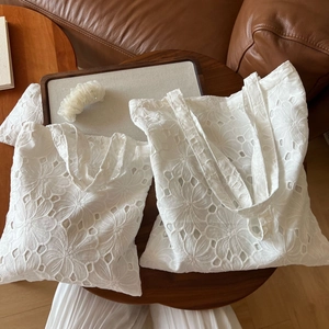 Detail of white cotton tote bags featuring intricate floral eyelet embroidery craftsmanship