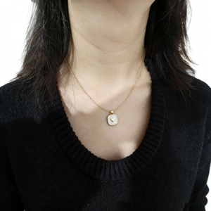 Dettaglio di una collana dorata con pendente quadrato a cuore indossata da una modella