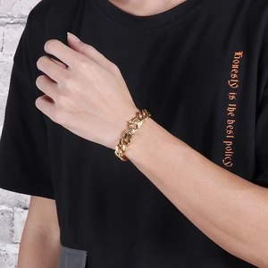 Detail of a gold Cuban link chain bracelet with embossed buckle on male wrist