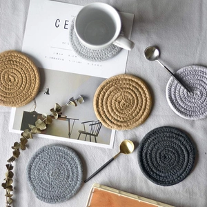 Top view of six woven cotton coasters in beige and gray on a rustic linen background