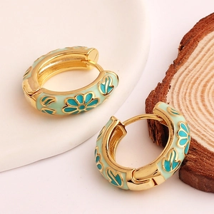 Close-up of mint green enamel flower earrings with blue floral pattern on gold hoops