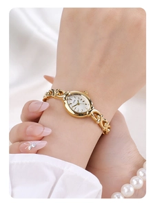 Gros plan d'une montre gourmette dorée avec cadran ovale et bracelet perle au poignet