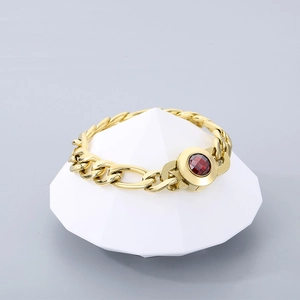 Detail of gold Cuban link bracelet featuring a faceted red gemstone inlaid in a round buckle