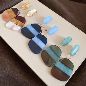 Detail view of multi-color acetate oval pendant earrings on white cards over plush fabric