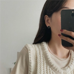 Detail showing a model wearing black heart stud earrings and a white pearl necklace