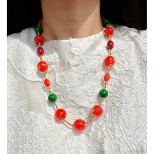 Handmade glass beaded necklace with red gold-foil and green beads on a white lace top