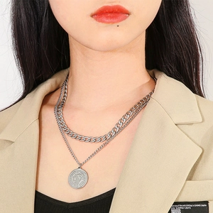 Detail of layered silver Cuban chain and vintage medallion pendant necklace on model neck