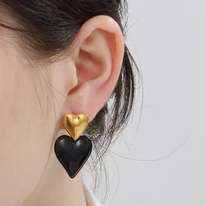 Close-up of dual heart earrings in gold and black, worn by a model for detail