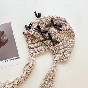 Elegante beige Strickmütze für Damen mit dunklen Lederschleifen und langen Quasten.