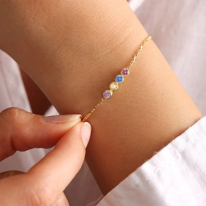 Gold chain bracelet featuring four colorful round gemstones on model's wrist
