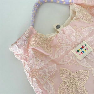 Gros plan sur les broderies papillon et l'étiquette de marque d'un sac à main rose