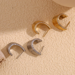 Macro detail of C-shaped 18K gold earrings with layered wave textures and micro-pavé diamonds