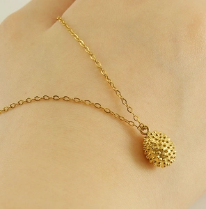 Detail of 18k gold plated durian pendant necklace on skin showing textured metal craft