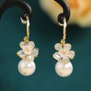 Macro detail of elegant pearl earrings with gold flower charms and crystals