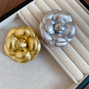 Close-up of elegant gold and silver camellia brooches with metallic textured leather petals