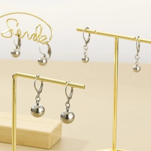 Detailed view of silver stainless steel ball earrings on golden display stands