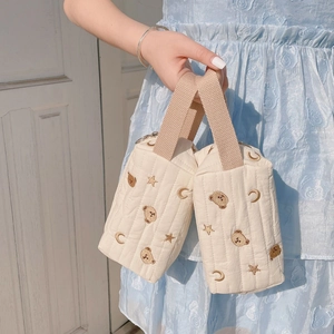 Close-up of quilted cream vanity bag with embroidered bears and stars held by a model
