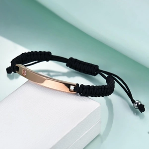 Detail of hand-woven black rope bracelet with rose gold bar and pink square zircon
