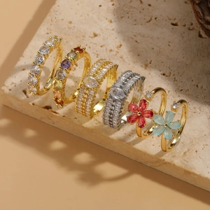 Dettaglio di anelli a fiore placcati oro 14K con zirconi colorati su vassoio in pietra