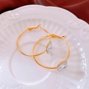 Detail of 24k gold plated hoop earrings with square zircon on white lace ceramic plate