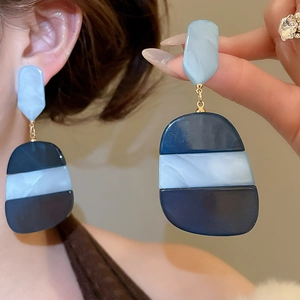 Detailed view of oversized blue oval acetate earrings with marble texture on model