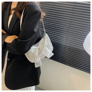Detail of white shoulder bag with mesh bow and decorative pearls on textured fabric