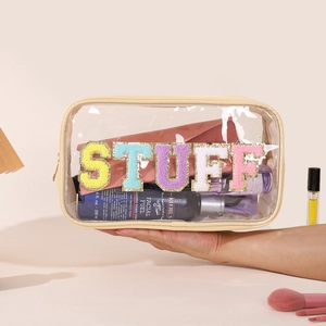 Close-up of a clear PVC toiletry bag featuring colorful sequin STUFF letters