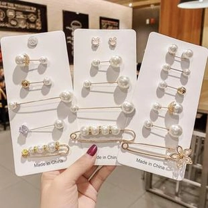 Close-up of assorted clover and pearl brooch pins displayed on cards in a hand
