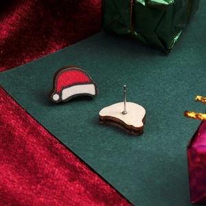 Detail view of wood Christmas hat stud earrings on festive dark green and red background