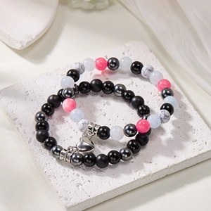 Detail of couple beaded bracelets with heart magnets on a white marble slab surface