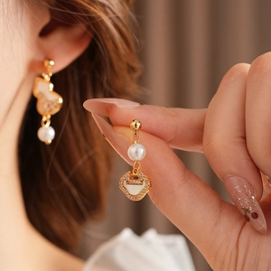 Detail of gold gourd drop earring with white pearl and zircon heart cutout in hand