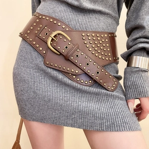 Detail of vintage brown leather belt with metal studs worn over a grey knit dress