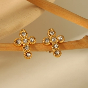 Gold cross earrings with white crystals on a wooden branch minimalist background