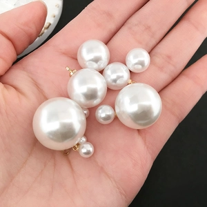 Handheld view of assorted white round pearls with gold metal loops for DIY jewelry making