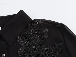 Close-up of elegant floral sequin embroidery on black chiffon blouse with gold button detail
