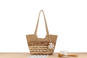 Detail of bohemian straw tote bag with intricate weave, floral charm, and long shoulder strap