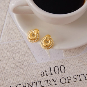 Detailed macro view of gold-plated twisted earrings with pavé crystals on a coffee cup