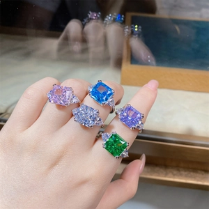 Close-up of five colorful square-cut silver rings featuring emerald and radiant gems