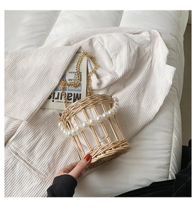 Detail of hand-woven straw bucket bag with pearl handle and metal chain on a white fabric